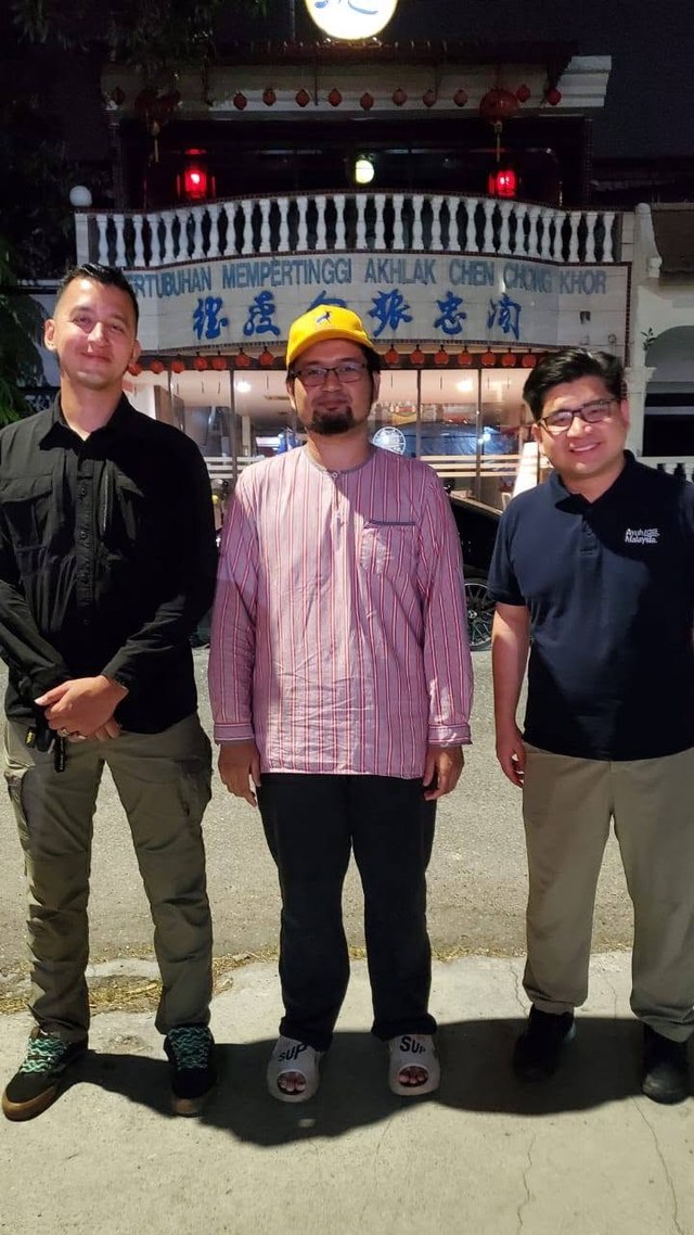 Aman Akil bergambar bersama dua rakan di hadapan bangunan pertubuhan pada malam program.