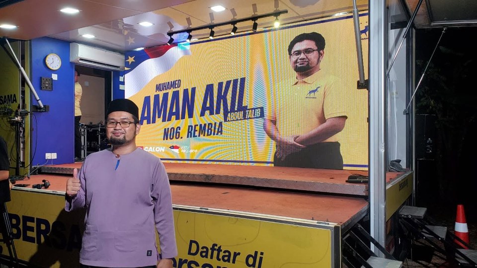 Foto di hadapan pentas Trak Kancil dengan paparan nama Aman Akil, N.06 Rembia.