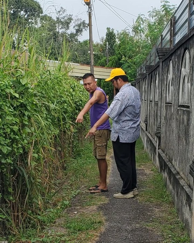 Aman Akil dan seorang penduduk menunjukkan keadaan tepi laluan yang dipenuhi tumbuhan.