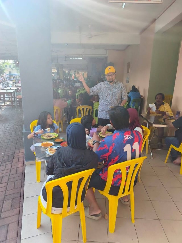 Aman Akil menyampaikan jemputan kepada pengunjung di sebuah kedai makan.
