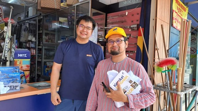 Aman Akil bergambar bersama seorang warga setempat di hadapan kedai sambil membawa risalah jemputan.