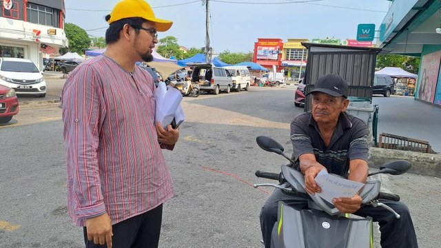 Aman Akil berbual dengan seorang penunggang motosikal yang memegang risalah jemputan.