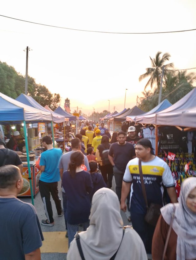 Pengunjung dan petugas BERSAMA di laluan pasar malam menjelang senja.