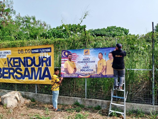 Ahli pasukan memasang sepanduk Kenduri BERSAMA dan sambutan kebangsaan pada pagar.