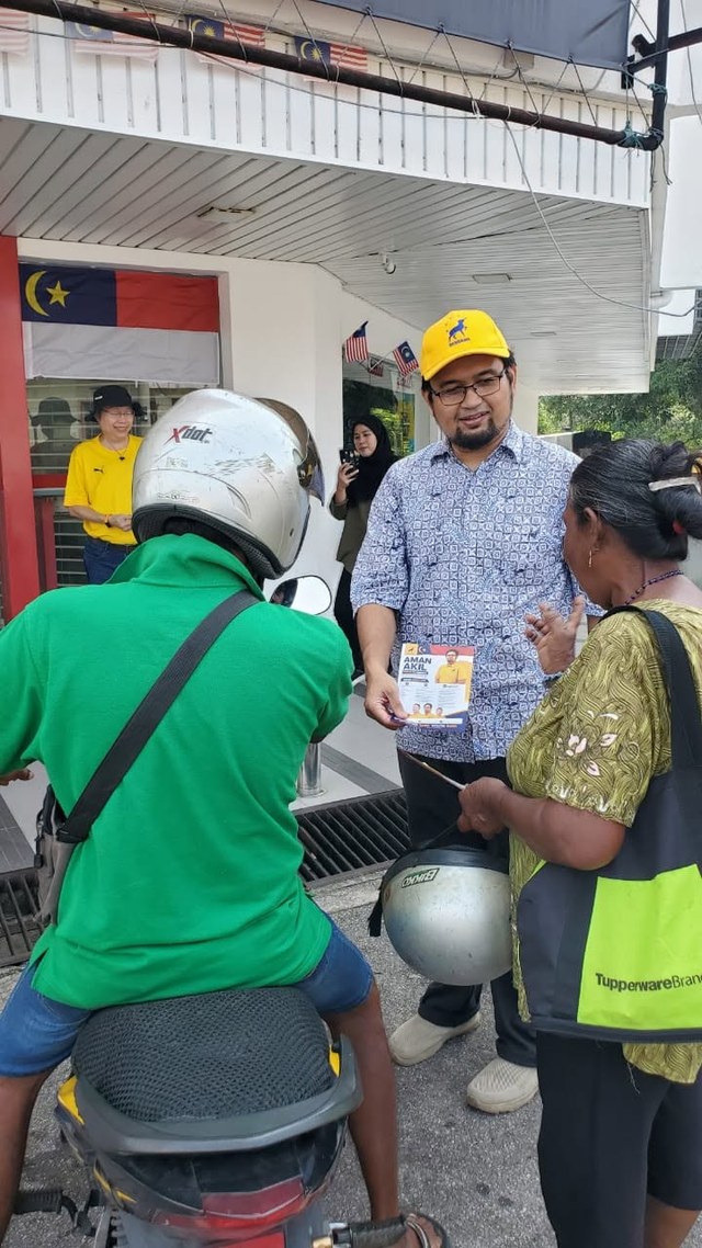 Aman Akil berbual dengan warga setempat berhampiran sebuah motosikal.